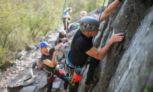 Beginning rock climber climbing a rock wall with assistance from his climbing instructor