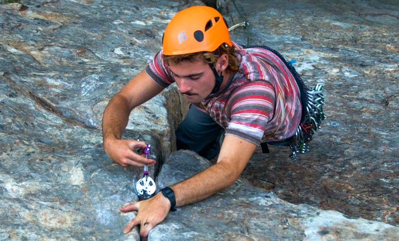 Young man learning to secure a rock climbing anchor into a crack in the wall