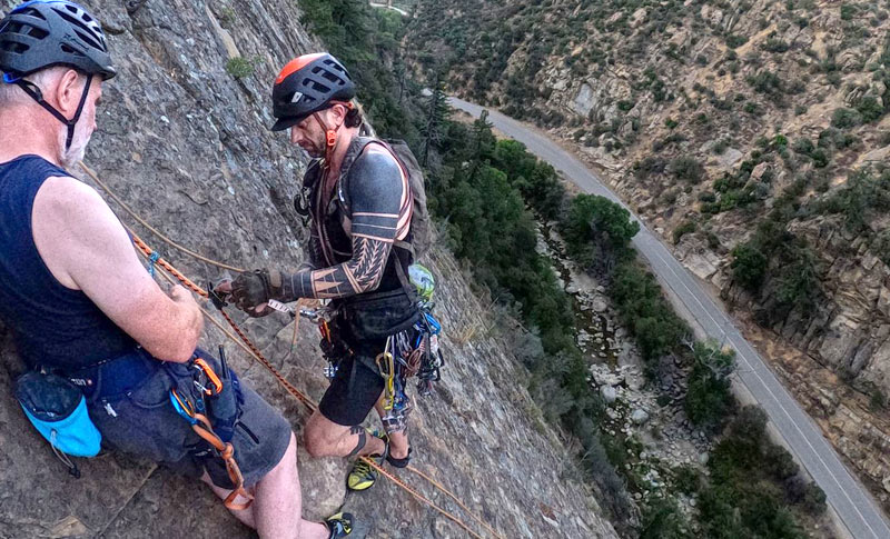 Rock climber, Alex Bury, shows a student how to secure a line to a bolt on a steep rock face.