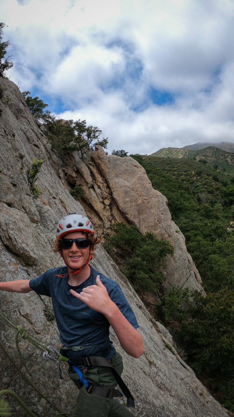 Smiling climber giving a shaka while ascending a sandstone ridge high above Santa Barbara’s coastal mountains.