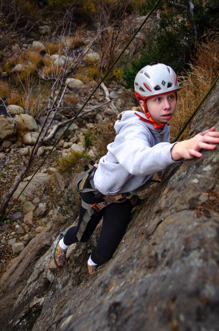 Young climber on a guided family rock climbing outing in Santa Barbara, safely ascending a sandstone wall with a helmet and harness.