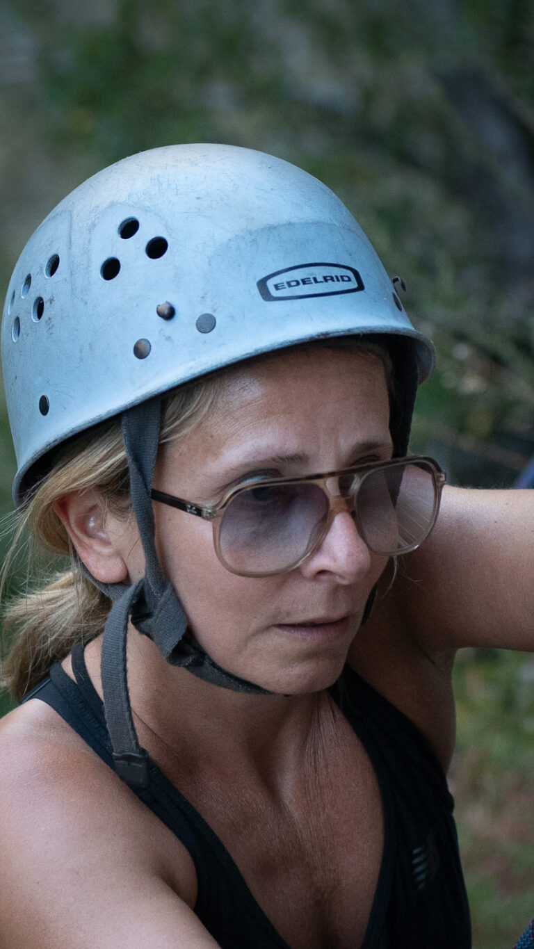Woman wearing a climbing helmet and glasses focusing intently while learning single-pitch climbing techniques in Santa Barbara.