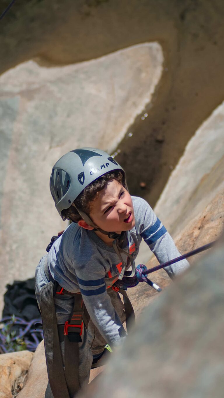 Young boy wearing a helmet and harness climbing a rock face during a guided Group Climbing Experience in Santa Barbara.